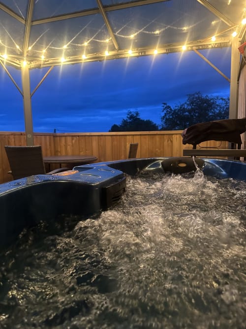 Bubbling hot tub on Dragonfly Pod balcony at dusk with garden views at Acorns Luxury Glamping, Holywell