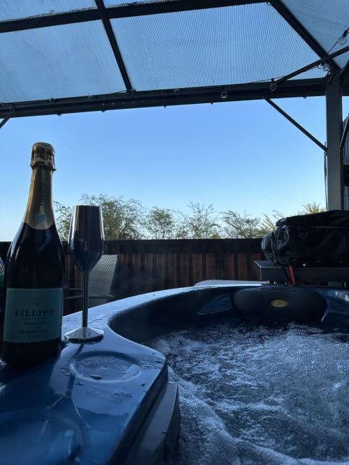 Champagne bottle and flute on table at Acorns Luxury Glamping Dragonfly Pod in Holywell with garden view