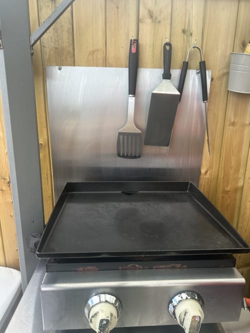 Stainless steel outdoor grill with cooking griddle and hanging BBQ utensils at Acorns Luxury Glamping in Holywell