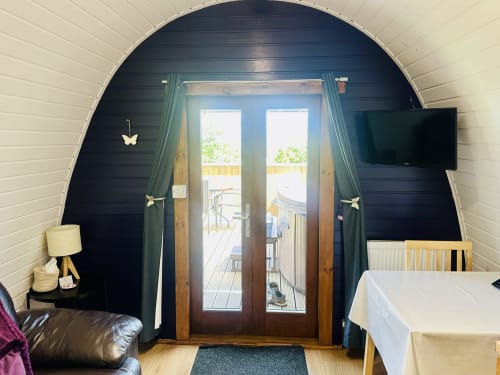 Butterfly Pod interior at Acorns Glamping with dark arched ceiling, French doors to garden balcony, and cozy furnishings