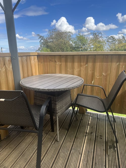 Outdoor balcony seating area at Acorns Luxury Glamping with round table, chairs, wooden railing, and garden views