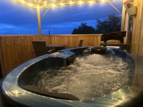 Bubbling hot tub on balcony at Acorns Luxury Glamping Butterfly Pod, Holywell, with garden views at twilight