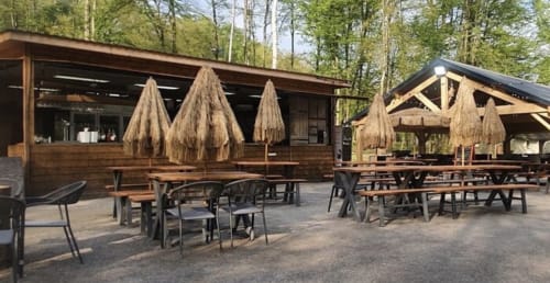 Espace de restauration en plein air des séjours Ardennais avec tables en bois, chaises et parasols à toiture de chaume à Renwez