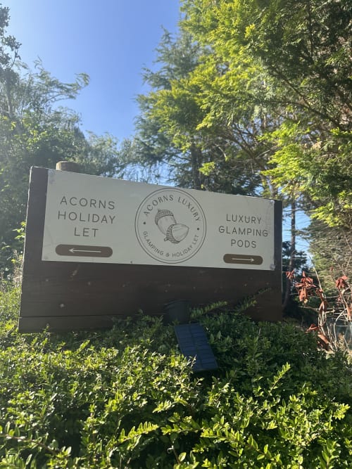 Acorns Luxury Glamping Pods roadside sign in Holywell surrounded by green trees and vegetation