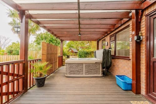 Covered garden deck with hot tub at Acorns Luxury Glamping, Holywell, featuring wooden pergola and brick cottage exterior