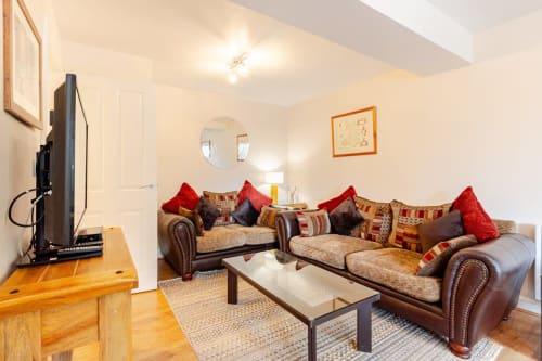 Luxury apartment sitting area at Acorns Glamping Holywell with leather sofas, red cushions, flat-screen TV, and wooden