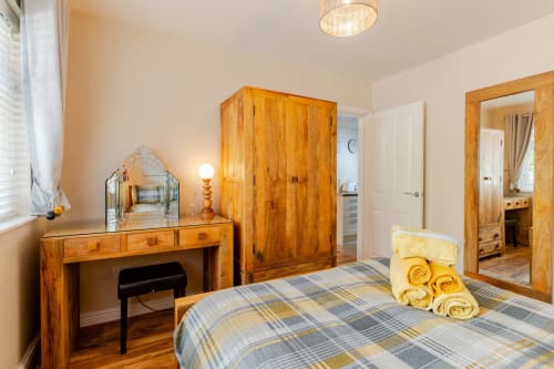 Spacious bedroom at Acorns Luxury Glamping with wooden wardrobe, vanity desk, plaid bedding, and garden view in Holywell