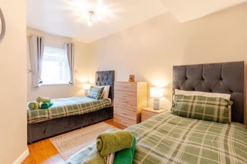 Bright bedroom at Acorns Luxury Glamping with two beds, green plaid bedding, grey headboards, wooden dresser, and warm