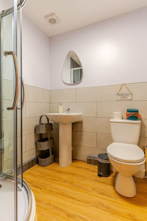 Modern bathroom at Acorns Luxury Glamping with wooden floors, cream tile wainscoting, pedestal sink, and shower area