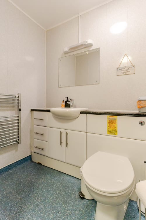 Modern bathroom at Acorns Luxury Glamping with white vanity, vessel sink, toilet, heated towel rack, and blue-tiled flooring