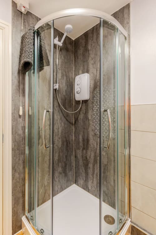 Modern shower enclosure with gray stone-effect walls and rainfall showerhead at Acorns Luxury Glamping, Holywell