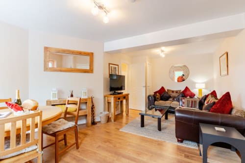 Spacious open-plan apartment at Acorns Luxury Glamping with wooden dining area, leather sofa, TV, and garden views in
