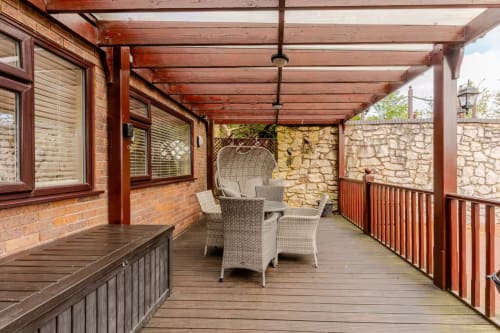 Wooden pergola balcony with wicker seating, stone walls, and garden views at Acorns Luxury Glamping, Holywell