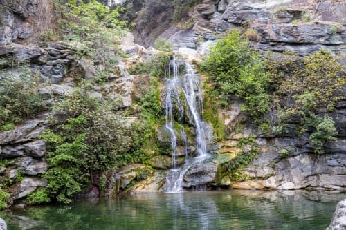 Cascade se déversant dans une piscine émeraude entourée de falaises rocheuses et de végétation luxuriante près de Linguizzetta, Corse