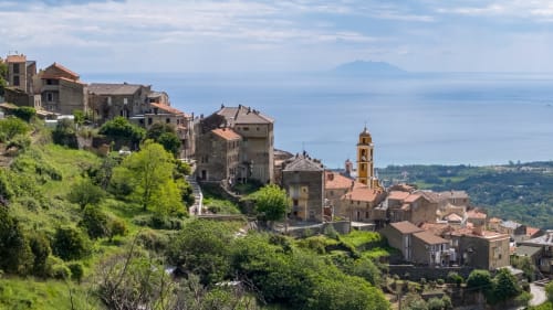 Village médiéval perché de Linguizzetta en Corse avec bâtiments en pierre, clocher et vue sur la mer