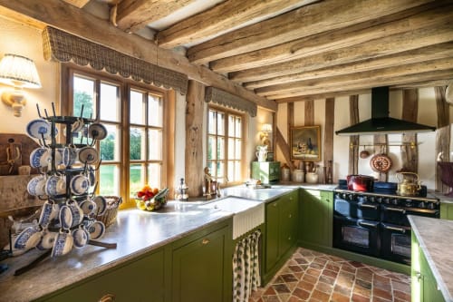 Cuisine fermière rustique aux armoires vertes, poutres apparentes et assiettes bleues décoratives à La Roquerie