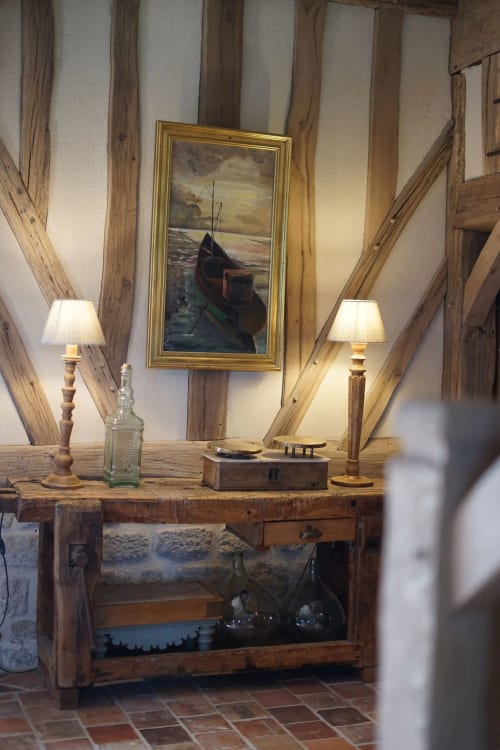 Intérieur rustique de la Ferme de La Roquerie avec poutres en bois, tableaux de bateaux, lampadaires et décoration avec vue sur lac
