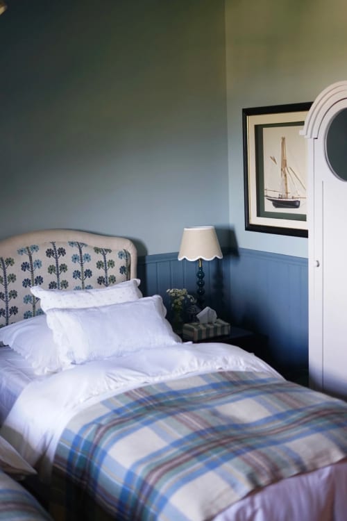 Chambre douillette à la Ferme de La Roquerie avec tête de lit nautique, parure bleue à carreaux et tableaux de voiliers