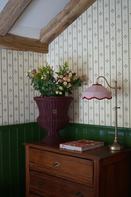 Coin enchanteur d'une chambre de campagne française avec papier peint floral, poutres en bois, jardinière en osier bordeaux fleurie