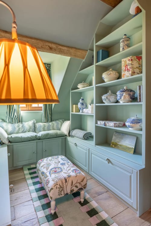 Coin lecture douillet aux étagères vert menthe, lampe suspendue orange et pouf à motifs à La Roquerie Farmhouse