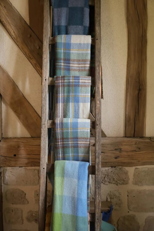 Serviettes écossaises pliées exposées sur une échelle en bois rustique dans une villa de la campagne française