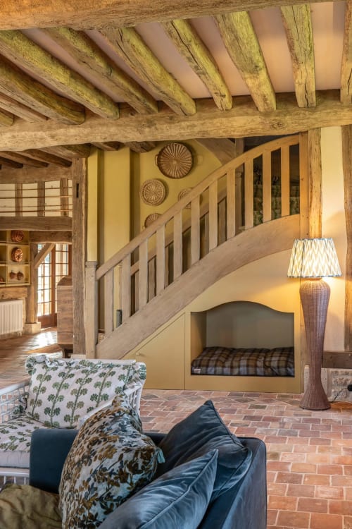 Intérieur de maison de campagne française rustique avec poutres en bois apparentes, murs jaunes, escalier et coin salon douillet