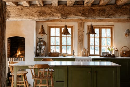 Cuisine rustique d'une ferme française avec armoires vertes, poutres apparentes, cheminée et suspensions en bois à La Roquerie