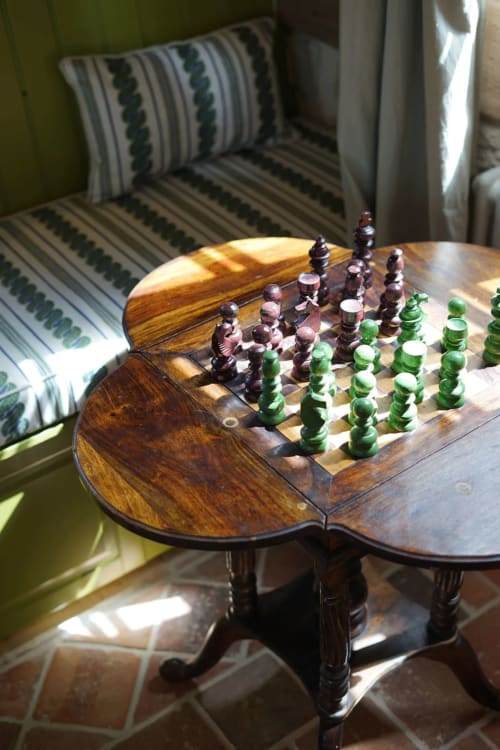 Jeu d'échecs en bois sur table ornée à la villa Mas de La Roquerie avec coussins rayés et vue sur la campagne