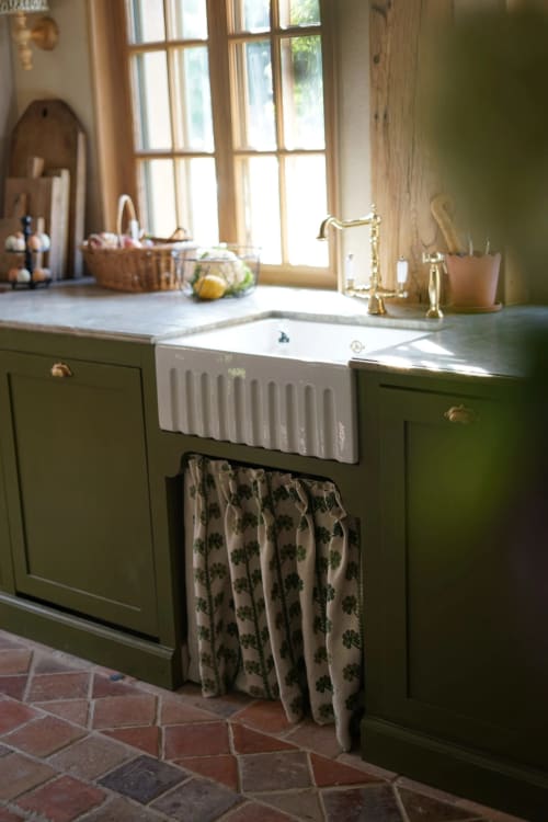 Cuisine de ferme française rustique avec mobilier vert sauge, évier blanc style fermier et détails de tissus aux motifs herbacés