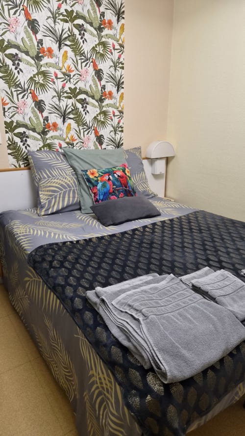 Chambre tropicale à l'hôtel Le Perroquet Bleu avec papier peint perroquets, literie à motifs et coussins décoratifs colorés