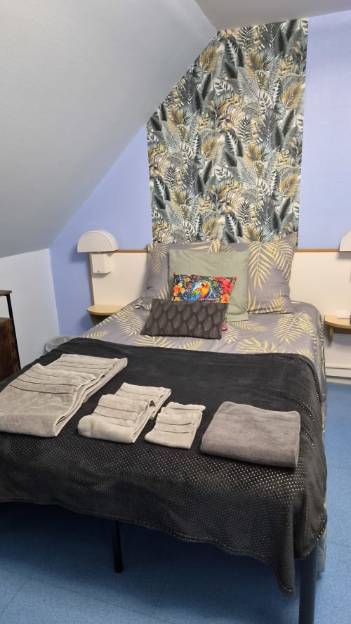 Chambre de l'Hôtel Le Perroquet Bleu avec serviettes pliées, literie tropicale et murs bleus à LA CHAPELLE BLANCHE ST MARTIN
