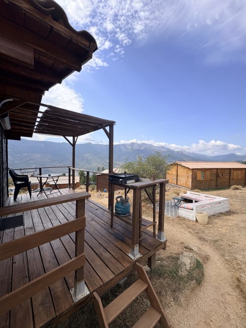 Terrasse en bois avec vue montagne aux Chalets de Lozzi, pergola, coin détente et chalets en rondins.