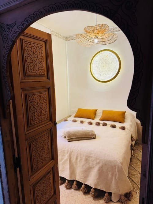 Chambre Stella Suite au Riad Casa Angelo avec porte en bois sculptée, plafonnier doré et literie crème avec touches moutarde