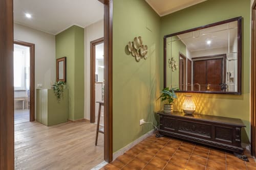Elegante corridoio in Family Boutique Flat vicino al Colosseo di Roma, con pareti verde salvia, mobili in legno scuro e specchi