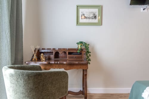 Elegante zona living nella Roma B&B con poltrona verde, scrivania in legno, opere d'arte incorniciate e dettagli decorativi