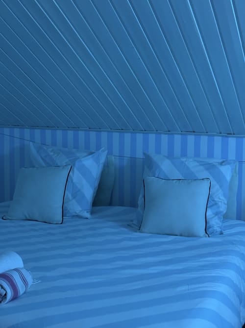 Bright blue bedroom with striped bedding, decorative pillows, and diagonal ceiling design at La Villa Maraloupia villa in Les