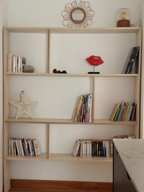 Light wood shelving unit in La Villa Maraloupia villa displaying books, decorative starfish, red lips sculpture, and woven