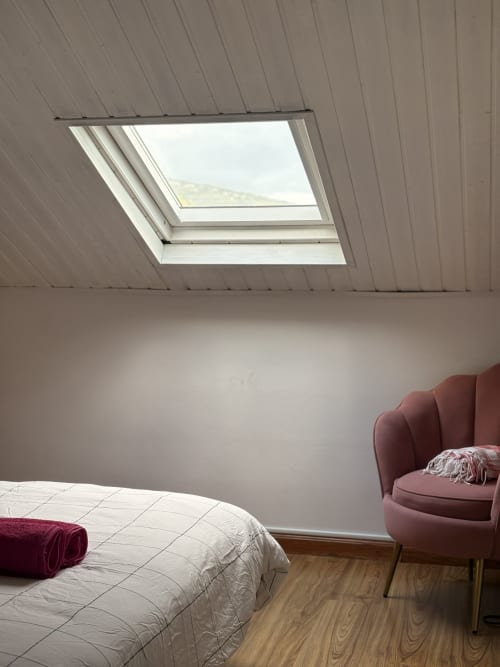 Modern bedroom with skylight window overlooking sea view, bed with white bedding, burgundy armchair, wooden floor at La Villa