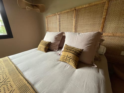 Chambre accueillante chez Nomads Togo avec literie blanche, tête de lit en rotin tressé et coussins décorativs moutarde à Lomé