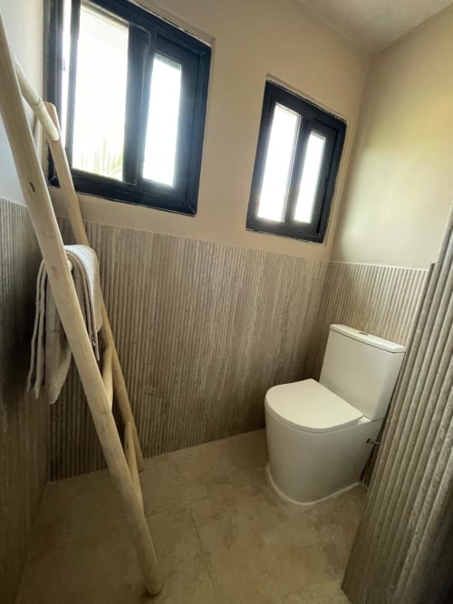 Salle de bain moderne à Nomads Togo Agbalepedogan à Lomé avec toilettes blanches, murs beige texturés, lumière naturelle et porte-serviettes