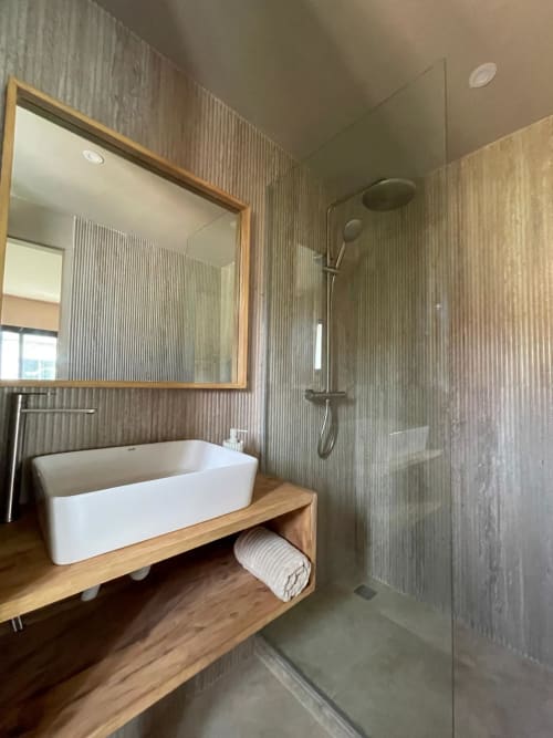 Salle de bain moderne à Nomads Togo avec vasque blanche, meuble bois, douche cascade et carrelage texturé
