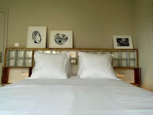 Chambre Nomads Togo Agbalepedogan avec literie blanche, tête de lit en bois et panneaux vitrés, décoration murale en noir et blanc encadrée