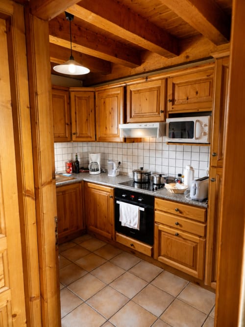 Rustic wooden kitchen in Le Chalet des Cimes apartment with pine cabinetry, black stove, and white tile backsplash