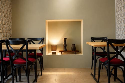 Élégante salle à manger au Au Bon Séjour avec chaises de bistro noires, coussins rouges et niche murale illuminée