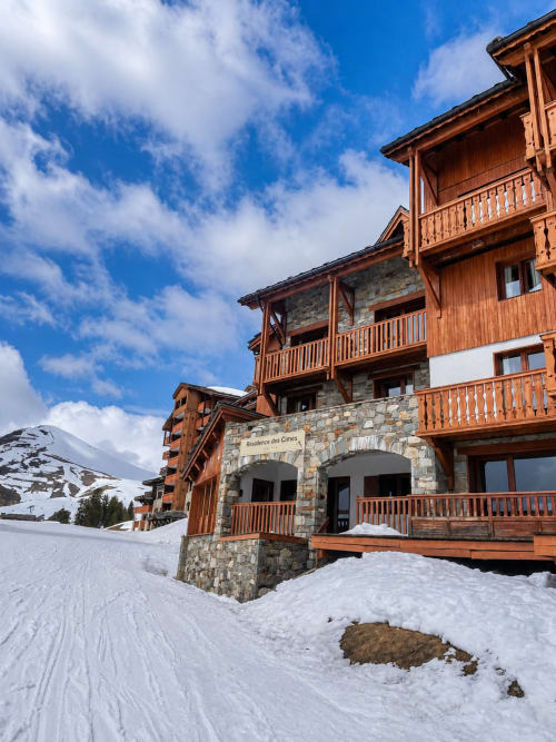 Le Chalet des Cimes in Belle Plagne: wooden and stone alpine resort building with snow-covered mountain slopes and clear blue