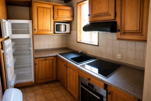 Wooden kitchen with electric cooktop, microwave, and open refrigerator in Le Chalet des Cimes apartment, Belle Plagne