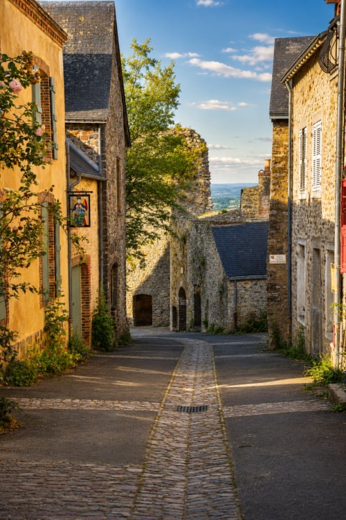 Charmante ruelle pavée de Sainte-Suzanne avec maisons en pierre et vue sur la vallée
