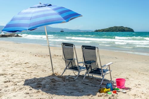 Guarda-sol listrado azul com duas espreguiçadeiras e brinquedos de praia na areias de Canasvieiras, Florianópolis, com águas turquesas