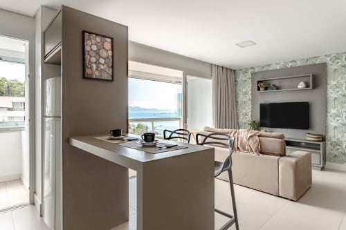 Apartamento moderno à beira-mar em Florianópolis com bancada na cozinha, vista para o mar da varanda, TV de tela plana e design contemporâneo