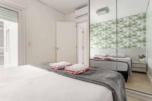 Quarto moderno em apartamento de Canasvieiras com guarda-roupa espelhado, papel de parede com vista do mar e camas preparadas com detalhes vermelhos